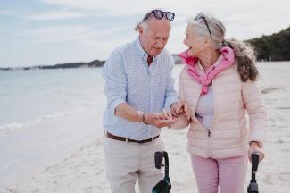 older man and woman with walker laughing alongside the beach