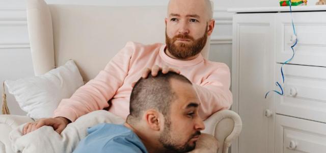 A gay male couple with sad facial expressions sitting in their child’s bedroom.